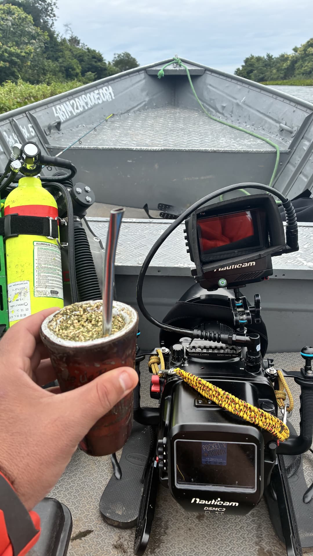 Hand holding a gourd of tereré next to underwater camera gear in a boat